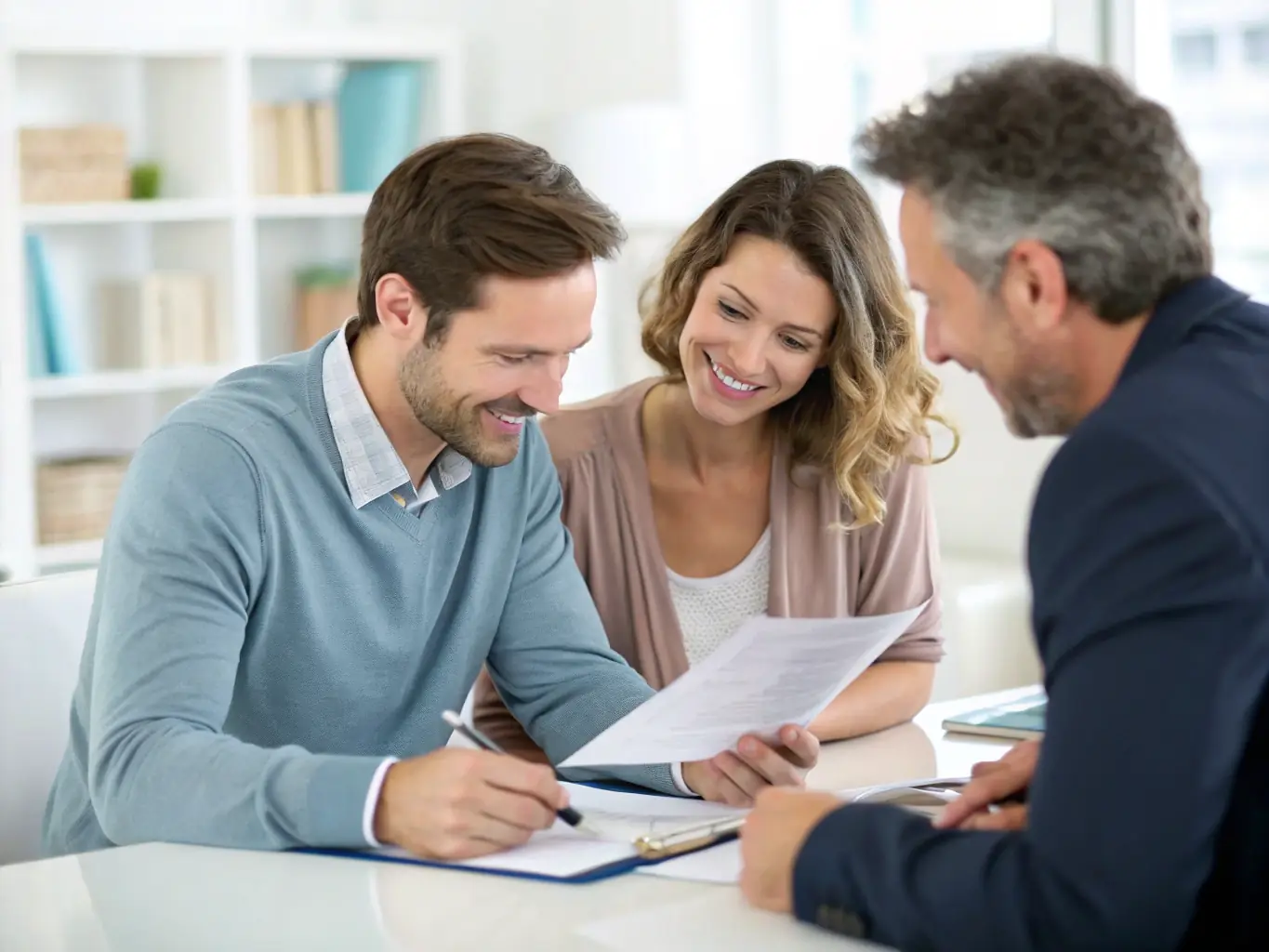 A couple reviewing their financial plan with a consultant, with documents and a laptop on the table, illustrating detailed financial planning services.